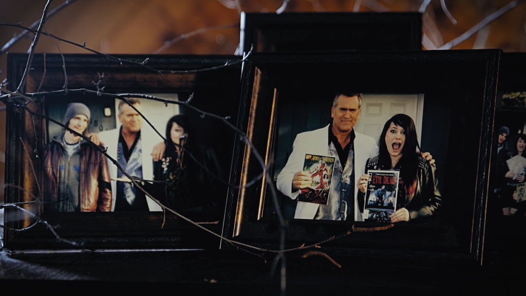 A still from documentary 'Hail to the Deadites'. The image shows two photo frames on a mantel piece with a piece of twig coming out from the left hand side. The images in the frames show Bruce Campbell, star of Evil Dead, at conventions meeting fans.